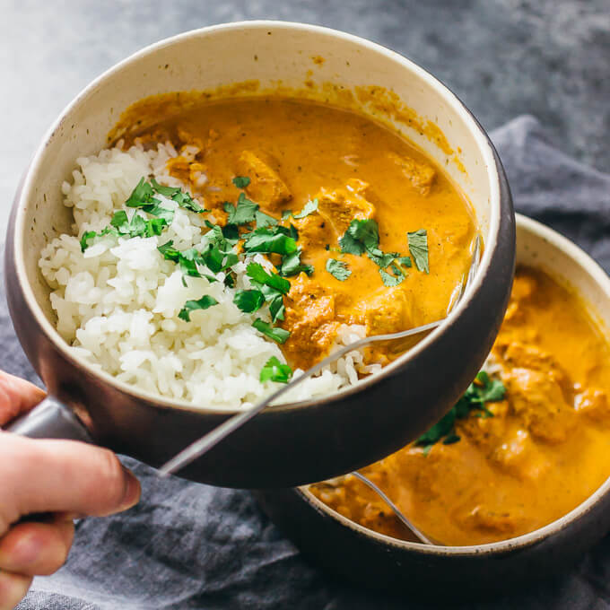 holding up a bowl with chicken tikka masala and rice